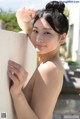 A naked asian woman leaning against a wall.