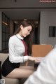 A woman in a white shirt and red tie sitting at a desk.