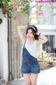 A woman in a white tank top and denim overalls posing for a picture.