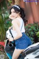 A woman in a white tank top and denim shorts sitting on a motorcycle.