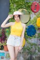 A woman in a yellow tank top and denim shorts posing for a picture.