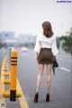 A woman in a white blouse and brown skirt is walking down the street.