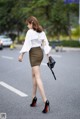 A woman walking down the street in a white blouse and brown skirt.