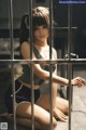 A woman sitting on the floor behind bars of a jail cell.