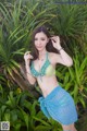 A woman in a bikini posing in front of a palm tree.