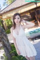 A woman in a white dress posing by a pool.