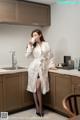 A woman in a bathrobe drinking from a cup in a kitchen.