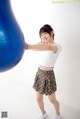 A woman in a white shirt and plaid skirt holding a blue ball.