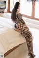 A woman in a black fishnet bodystocking sitting on a bed.