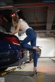 A woman leaning on the trunk of a blue car.