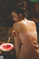 A woman in a pink tank top standing next to a bowl of watermelon.