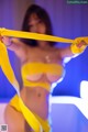 A woman in a yellow bikini holding a yellow ribbon.