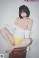 A woman in a white shirt and yellow panties sitting on a stool.