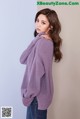 a woman wearing a purple sweater and jeans leaning against a wall