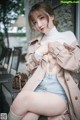 A woman sitting on a chair wearing a trench coat.