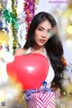 A woman holding a red heart shaped balloon in front of a Christmas tree.