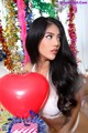 A woman holding a red heart shaped balloon in front of a Christmas tree.