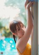 A woman in a yellow bikini leaning against a window.