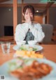 A woman sitting at a table with chopsticks in front of her face.