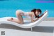 A woman in a white lingerie laying on a lounge chair by a pool.