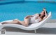 A woman in a white bathing suit laying on a lounge chair by a pool.