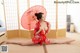 A woman in a red kimono sitting on the floor holding an umbrella.