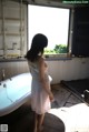 A woman in a white dress standing in front of a bathtub.