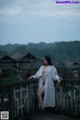 A woman in a white coat standing on a bridge.